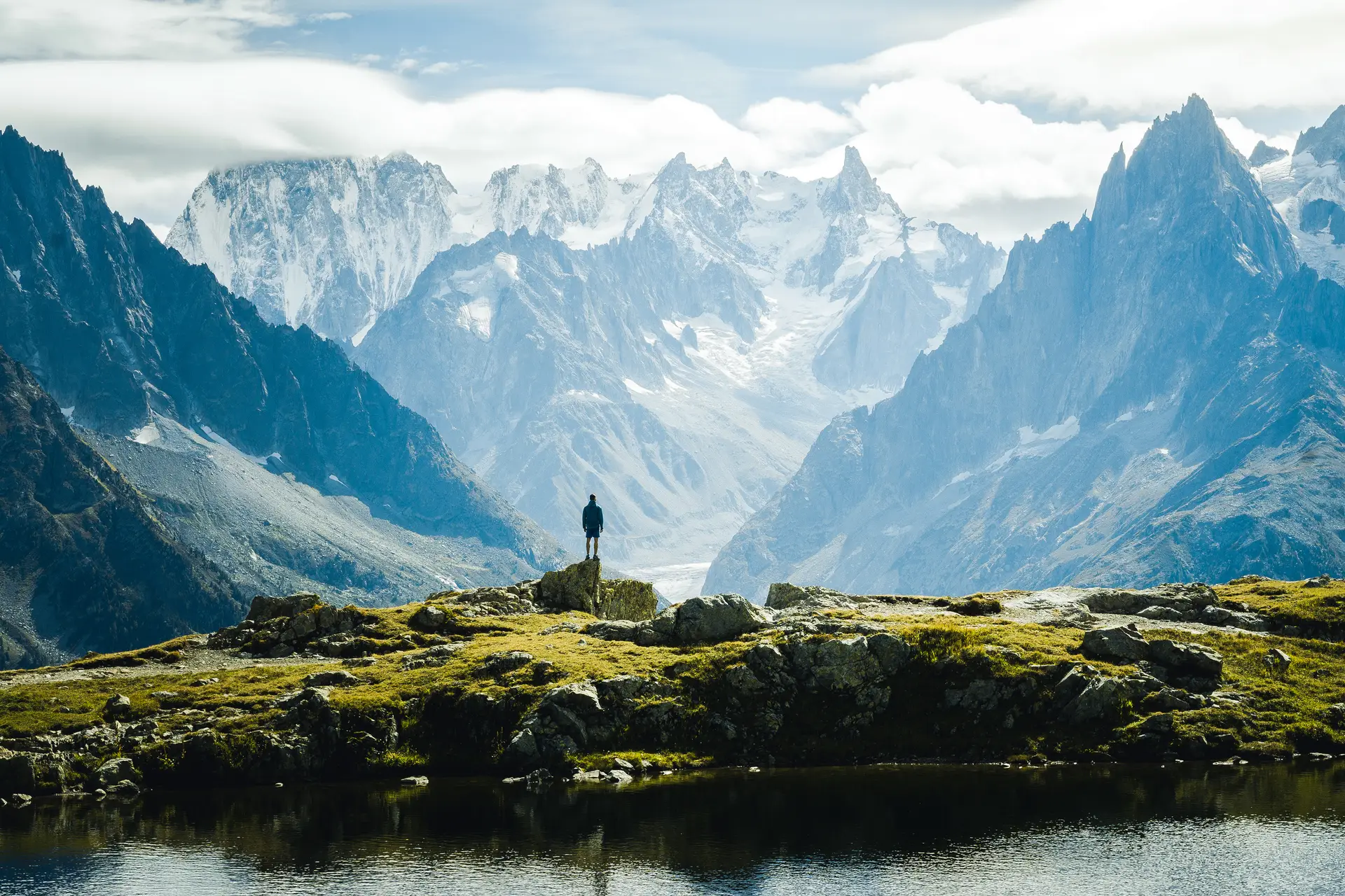 A distant hiker overlooking a lake and snow-covered mountain peaks