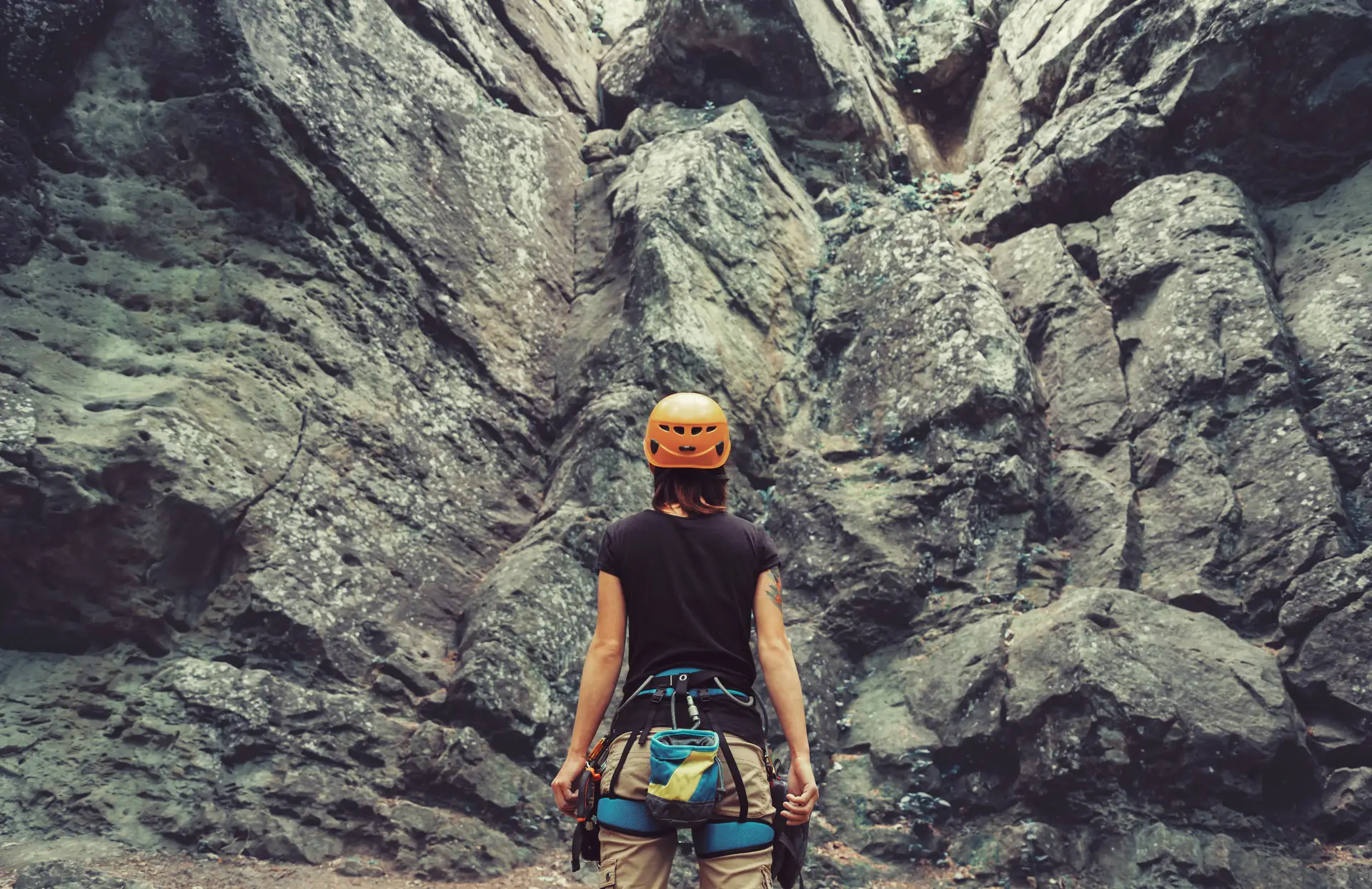 A climber wearing a helmet and harness, looking up at a rock face