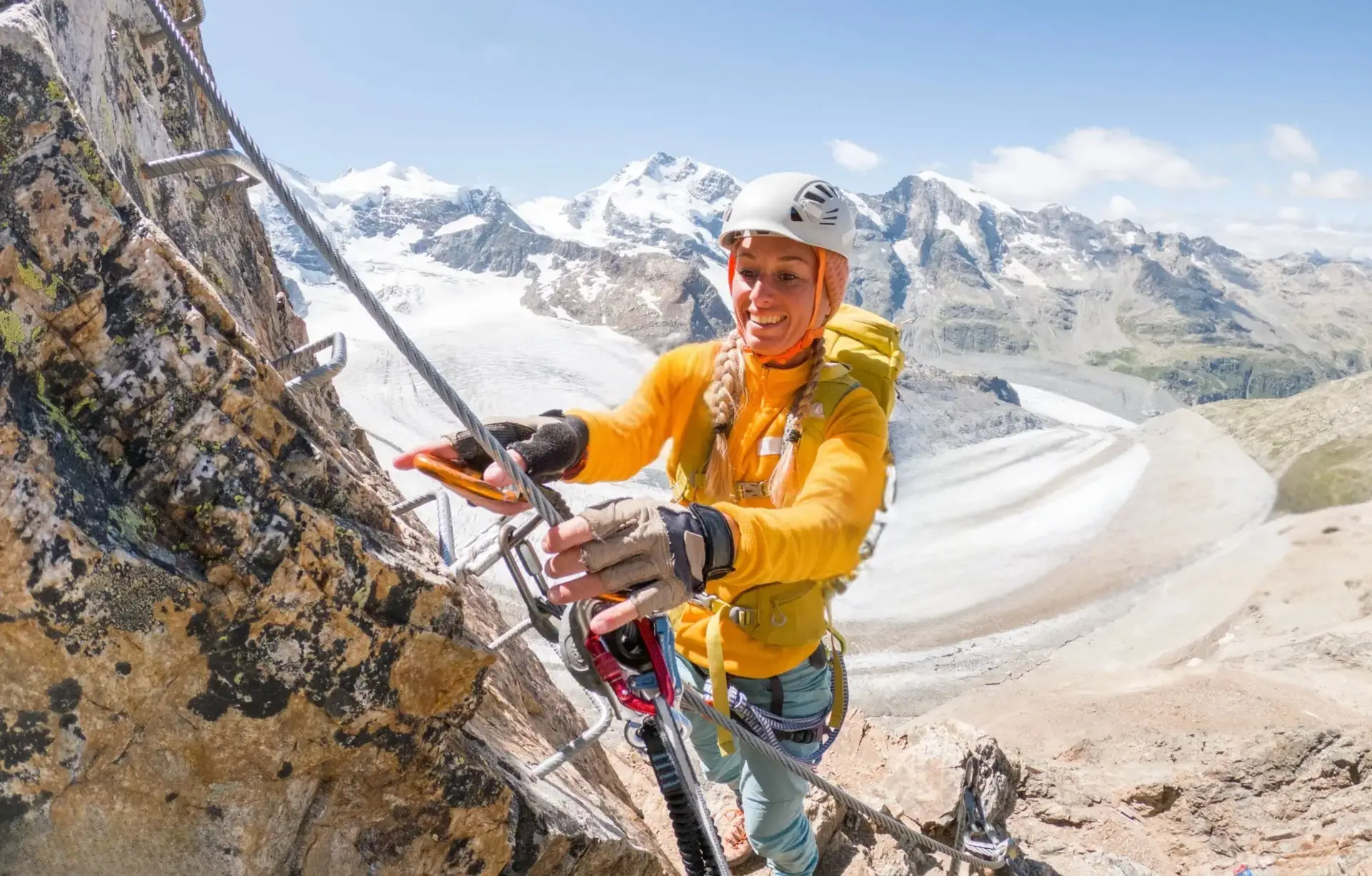 Woman climbing via ferrata in high alpine terrain with glacier in the background