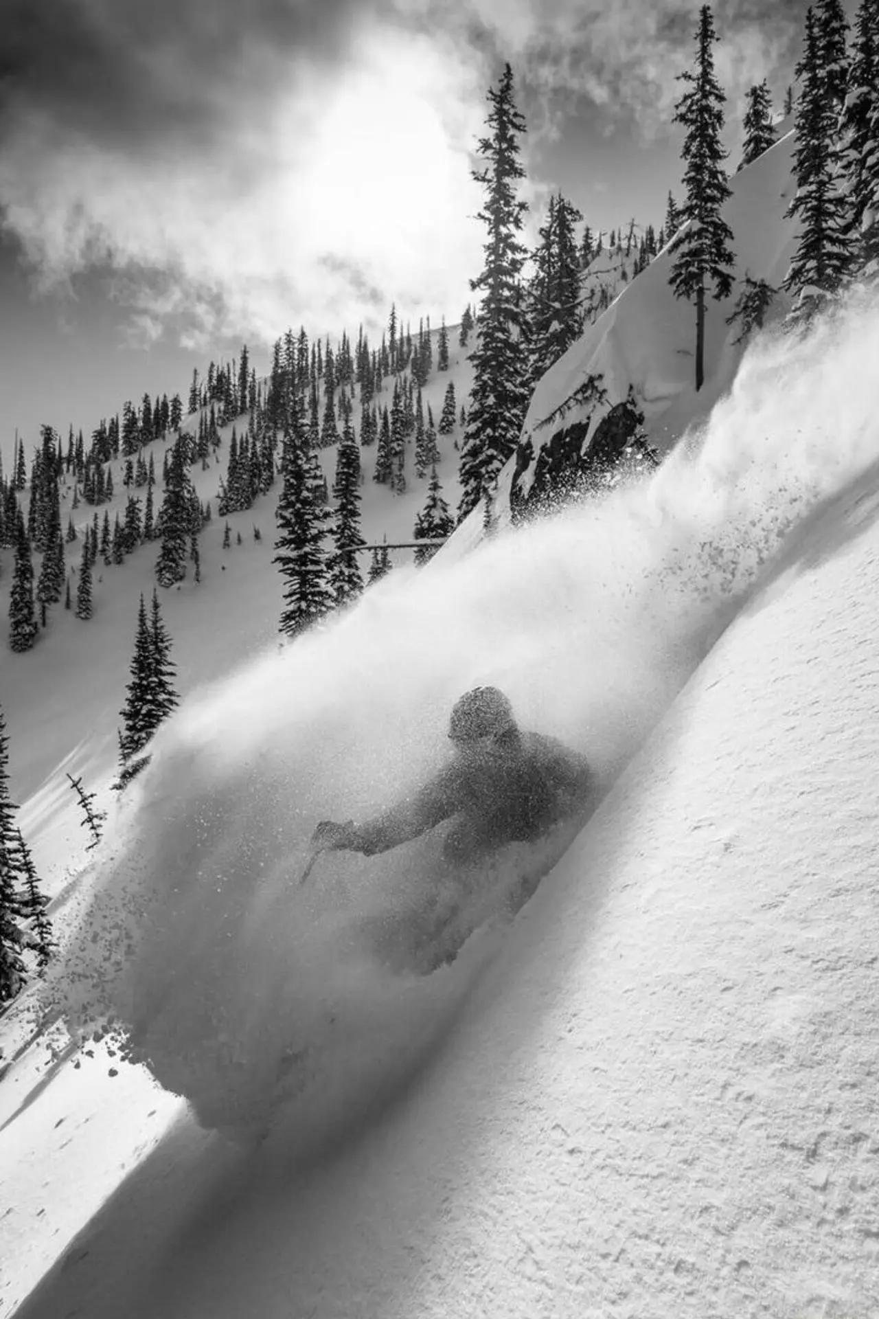 A skier moving through deep snow beneath a forested mountain slope